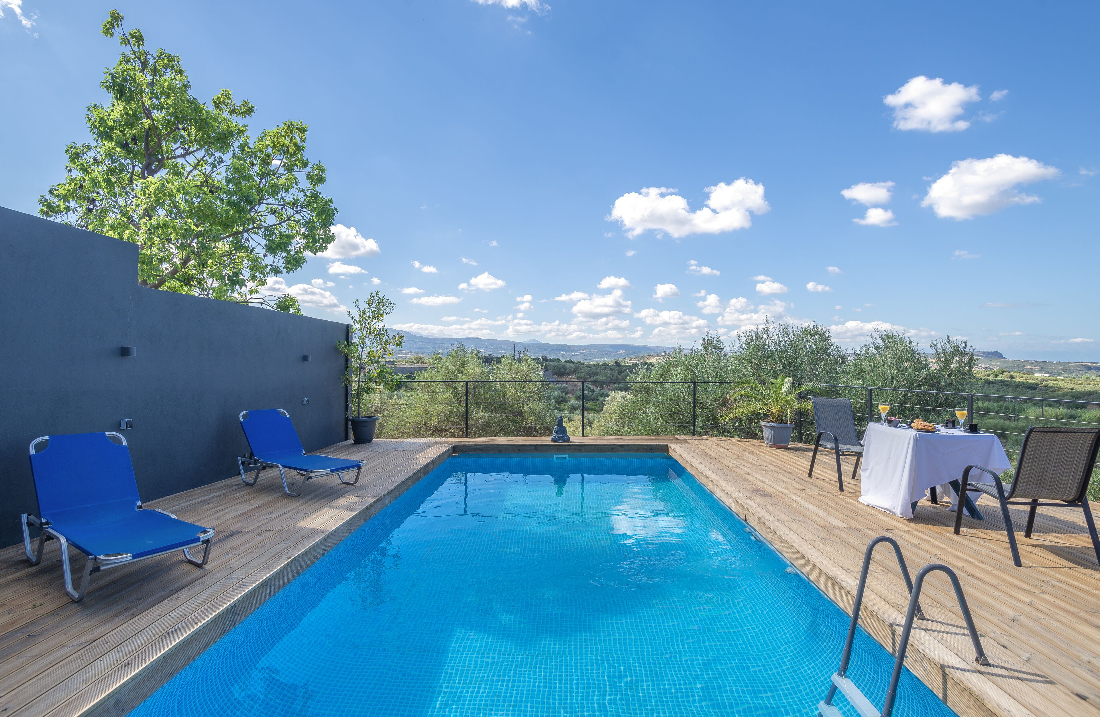 A swimming pool with blue tiles, surrounded by wooden deck and blue lounge chairs.