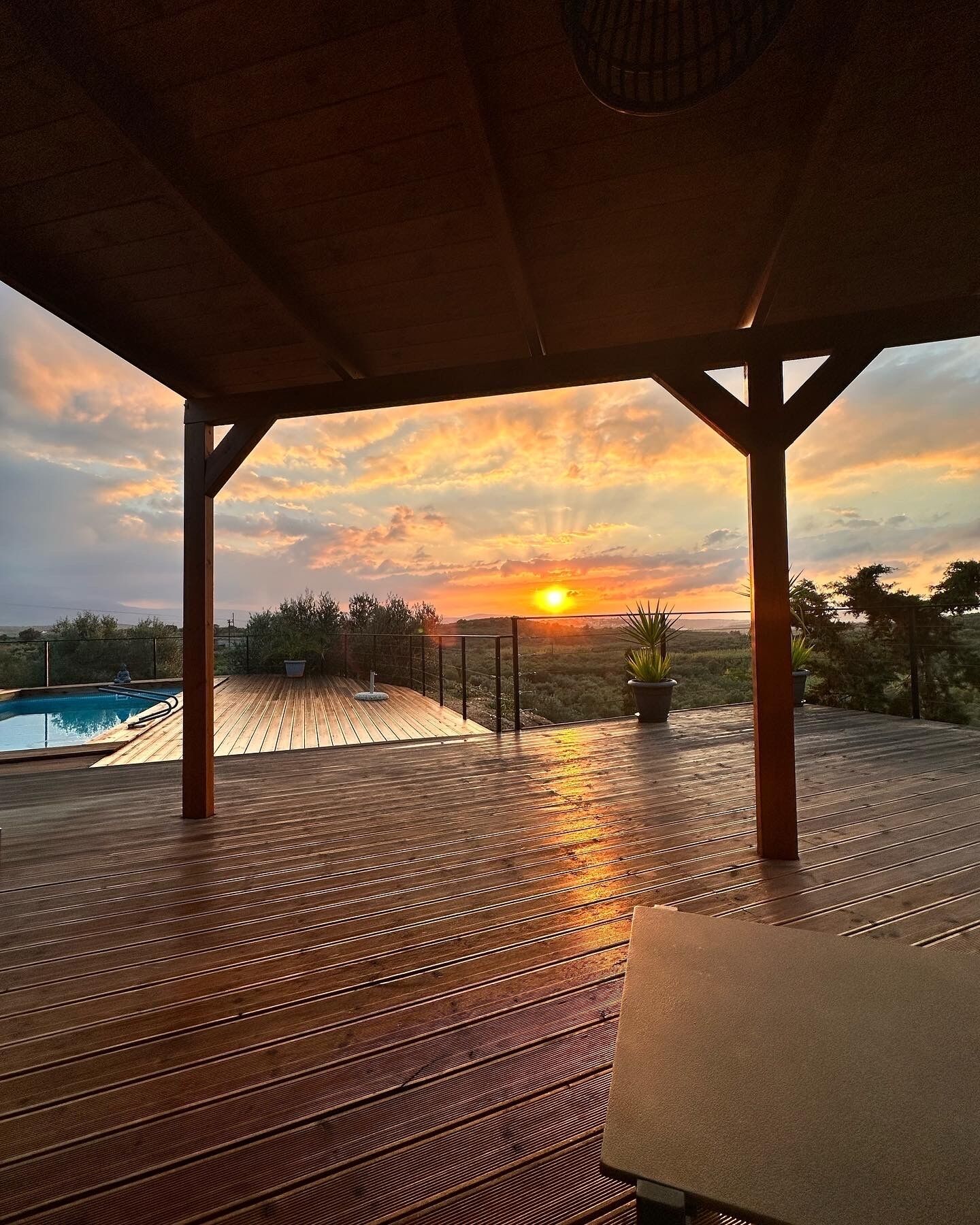 Eine Holzterrasse mit Blick auf den Sonnenuntergang über der Landschaft.