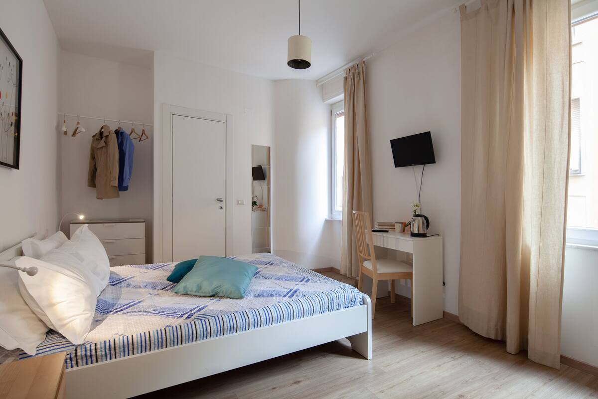 Um quarto com cama, escrivaninha, cadeira e televisão.