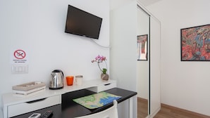 A modern hotel room with a desk, a flat-screen TV, a map, a coffee maker, a plant, and a painting on the wall. - Suites Colombo 32 (La Spezia)