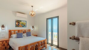 A bedroom with a wooden bed, a painting on the wall, a window with a view, and a towel rack. - Blue Sea Tower, Luxury Villa, Private Heated Pool and Gardens. Superb Ocean view (Fajã da Ovelha)