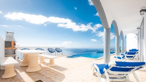 A terrace with a pool, lounge chairs, and tables overlooking the sea. - Blue Sea Tower, Luxury Villa, Private Heated Pool and Gardens. Superb Ocean view (Fajã da Ovelha)