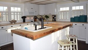 A modern kitchen with white cabinetry, a wooden island with a sink, and bar stools. - Sunny Claire- Beautiful In Town Cottage w/ Hot Tub (Chincoteague)