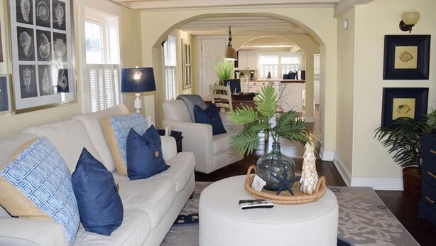 A living room with a sofa, coffee table, and a kitchen in the background. - Sunny Claire- Beautiful In Town Cottage w/ Hot Tub (Chincoteague)