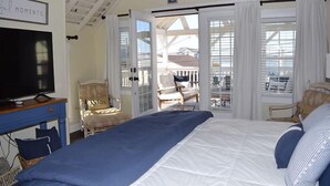 A bedroom with a bed, a television, a chair, and a balcony with a view. - Sunny Claire- Beautiful In Town Cottage w/ Hot Tub (Chincoteague)