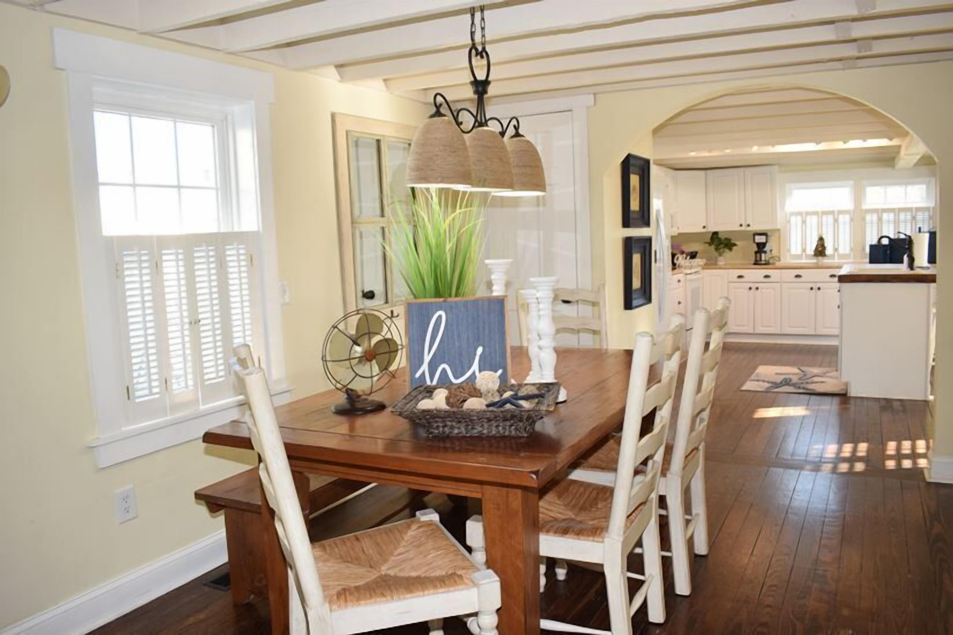 Un espace repas avec une table en bois, des chaises blanches et un luminaire suspendu.