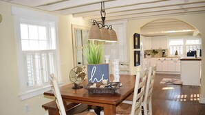 A dining area with a wooden table, white chairs, and a hanging light fixture. - Sunny Claire- Beautiful In Town Cottage w/ Hot Tub (Chincoteague)