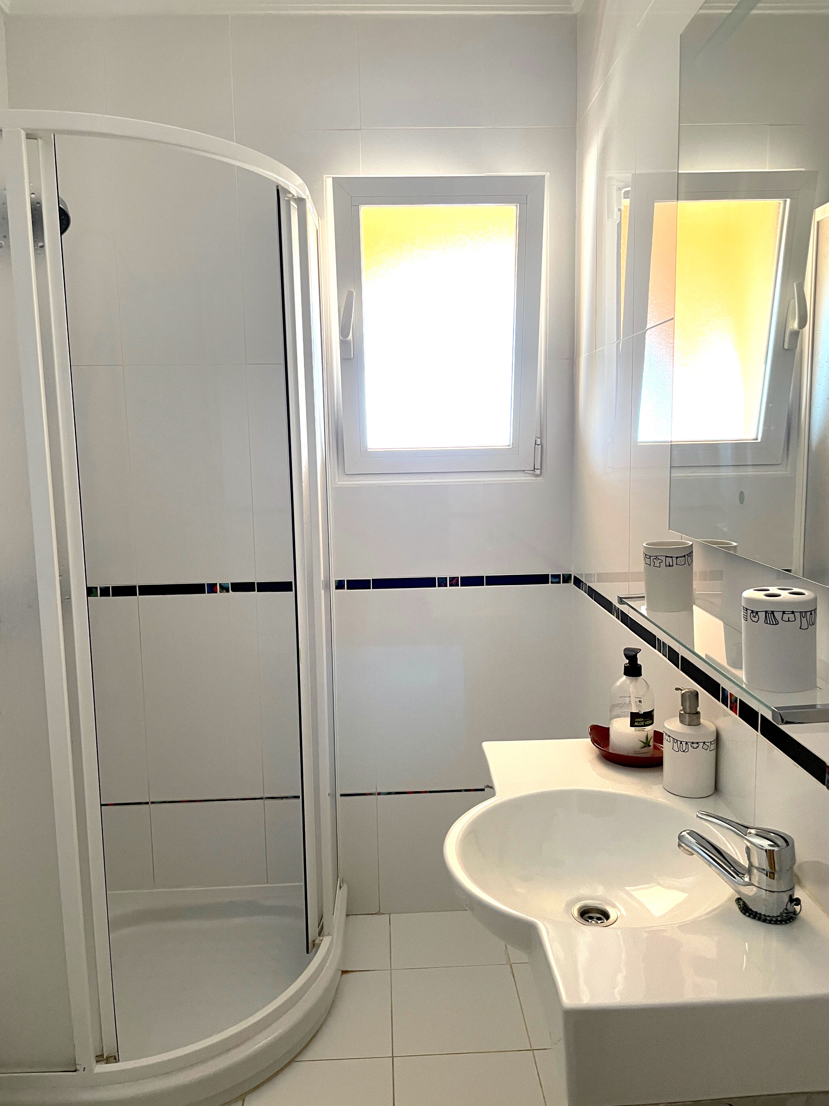 Een moderne badkamer met een douche, wastafel en raam.