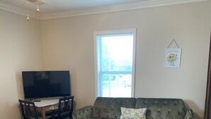 Ein Zimmer mit einem Bett, einem Holztisch, einem grünen Sofa, einem Fernseher und einem Fenster mit Jalousien.