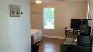 Ein Zimmer mit einem Bett, einem Fernseher, einem Schreibtisch und einem Fenster.
