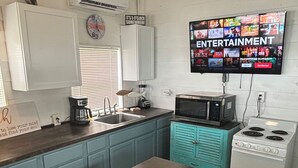 Une cuisine compacte avec une table en bois, des placards de couleur turquoise, un four à micro-ondes, une cuisinière et un téléviseur diffusant des chaînes de divertissement.