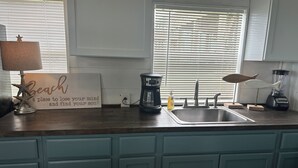 Une cuisine avec un plan de travail en bois, une machine à café, un mixeur et un panneau sur lequel on peut lire : « La plage, un endroit pour se vider l’esprit et retrouver son âme. »