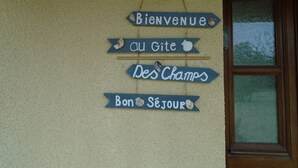 A wall with signs reading "Bienvenue," "Au Gîte," "Des Champs," and "Bon Séjour," indicating a welcoming sign for guests.
