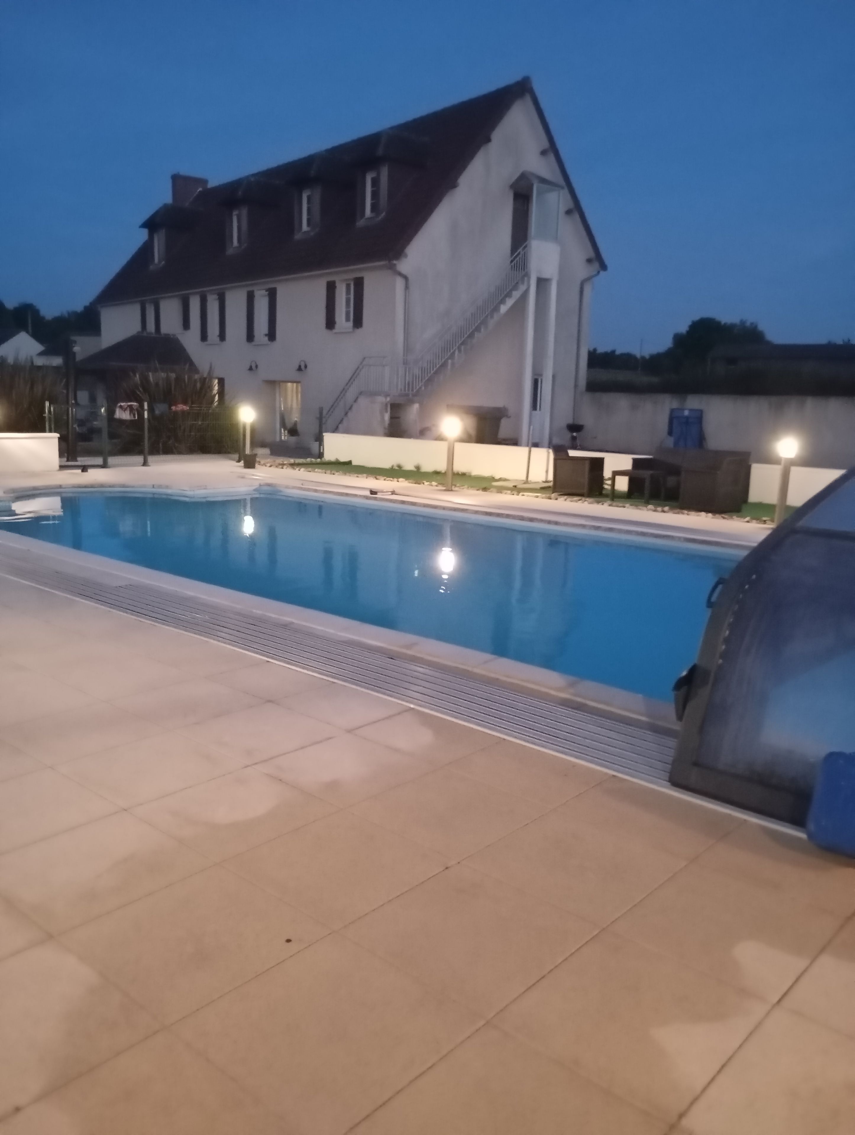 Une piscine avec une terrasse carrelée, un escalier menant à un bâtiment et une voiture garée à proximité.