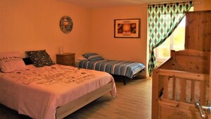 A bedroom with a large bed, a smaller bed, a nightstand, a mirror, a framed picture, and a window with curtains.