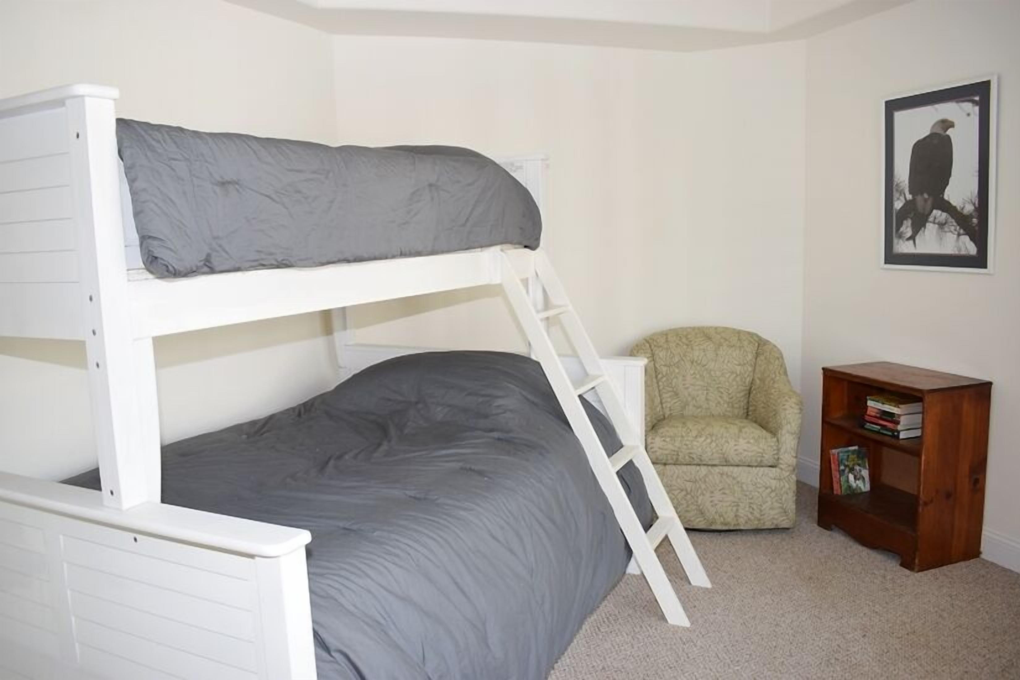 A bunk bed with a ladder, a chair, and a small wooden side table with books.
