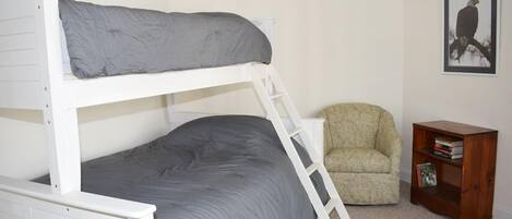 A bunk bed with a ladder, a chair, and a small wooden side table with books.