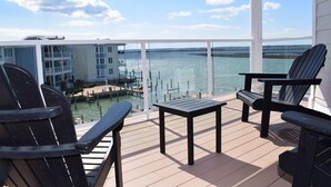 Una terraza con dos sillas Adirondack y una mesita, con vistas a un puerto deportivo con barcos y un edificio al fondo.