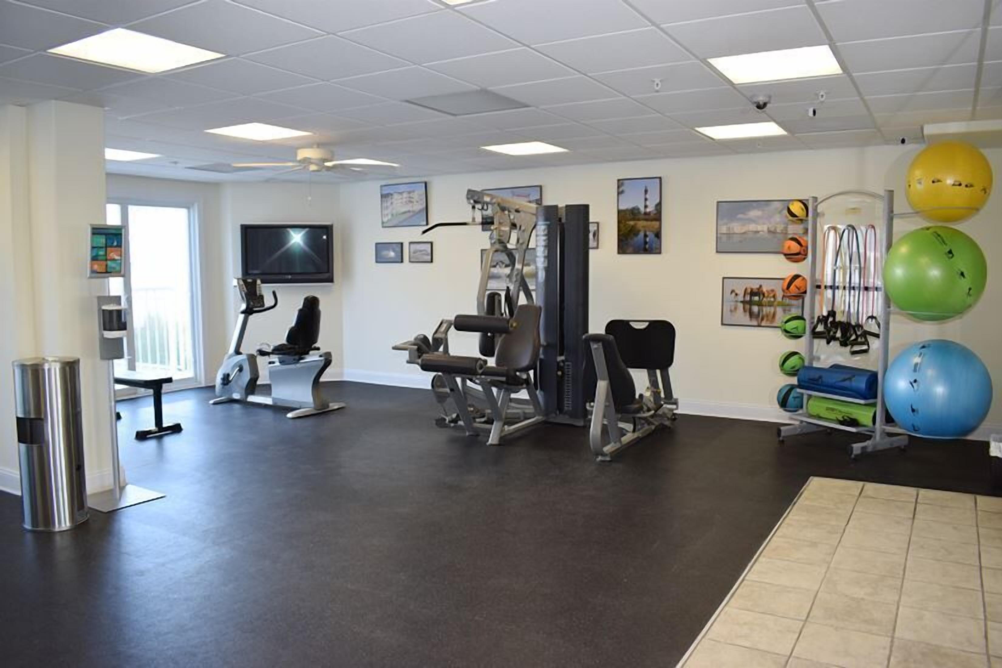 Un gimnasio con equipo de ejercicio, un televisor y pelotas de ejercicio en la pared.