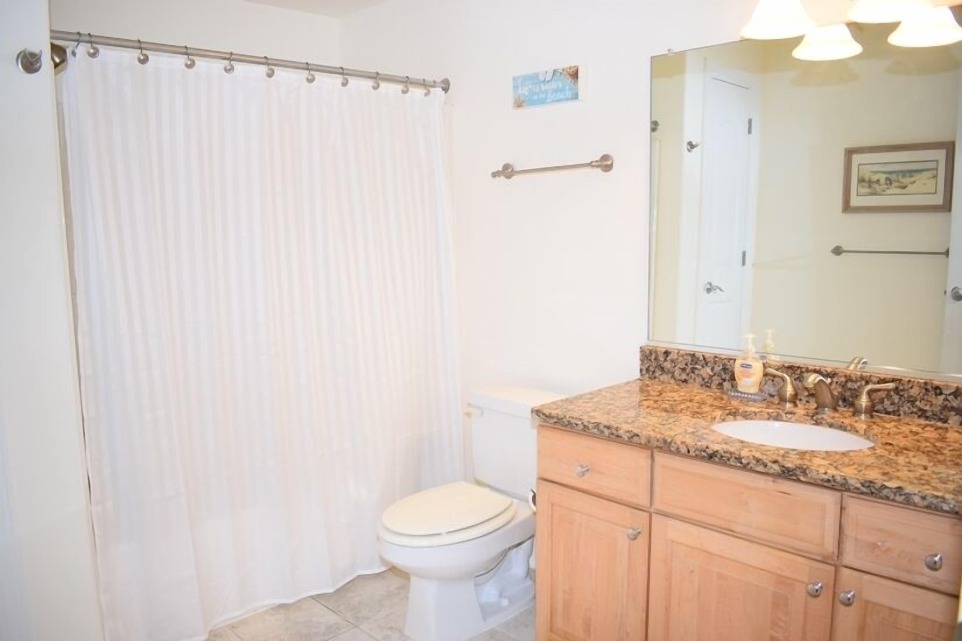 A bathroom with a toilet, sink, vanity, and a shower curtain.