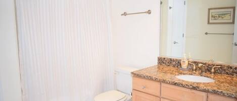 A bathroom with a toilet, sink, vanity, and a shower curtain.