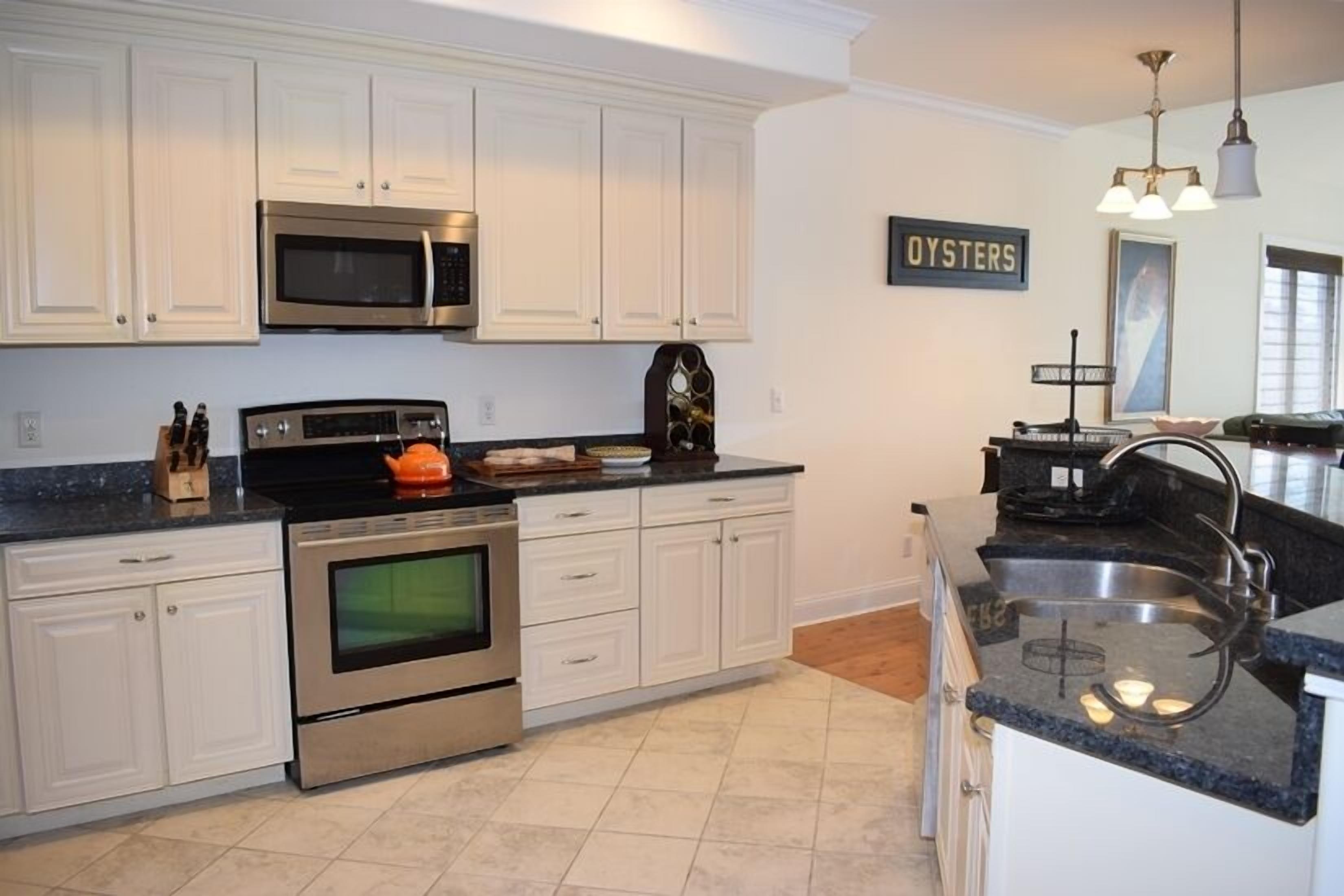 A modern kitchen with white cabinets, stainless steel appliances, and a black countertop.