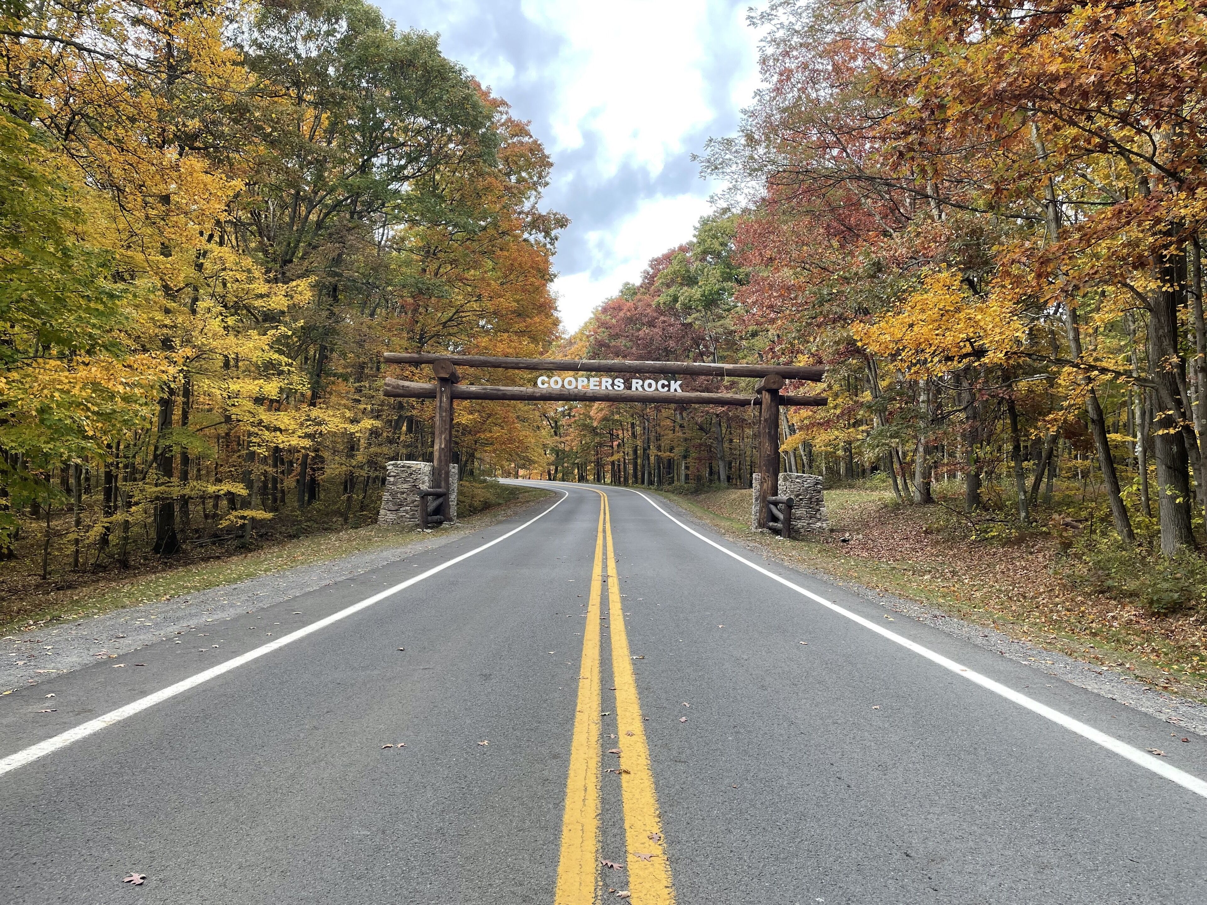 Une route menant à un panneau indicateur sur lequel on peut lire « COOPER’S ROCK », le tout étant entouré d’arbres aux couleurs automnales.