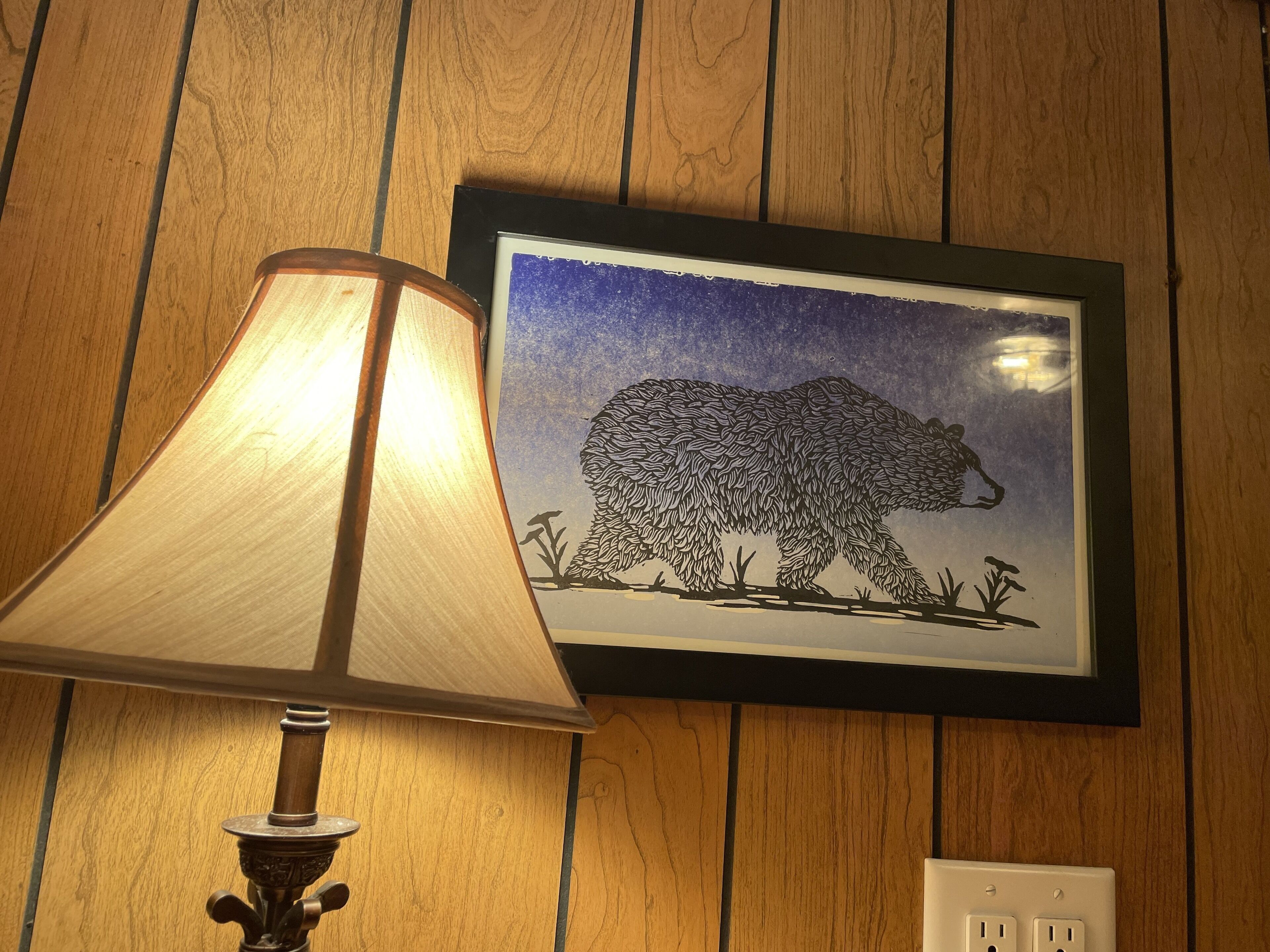A wall-mounted lamp with a wooden shade and a framed bear silhouette artwork.