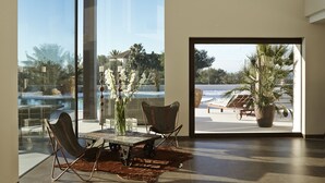 Una habitación amplia con ventanas grandes, un comedor con mesa y sillas, y vista a una piscina y palmeras afuera.