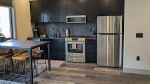 Une cuisine moderne avec des meubles de couleur sombre, des appareils en acier inoxydable, une table à manger en bois et des tabourets de bar.