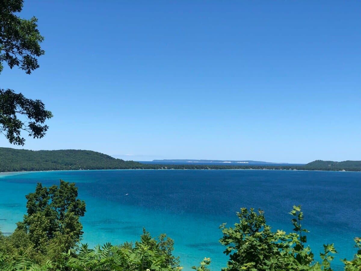 A coastal landscape with clear blue waters, dense greenery, and distant landforms.