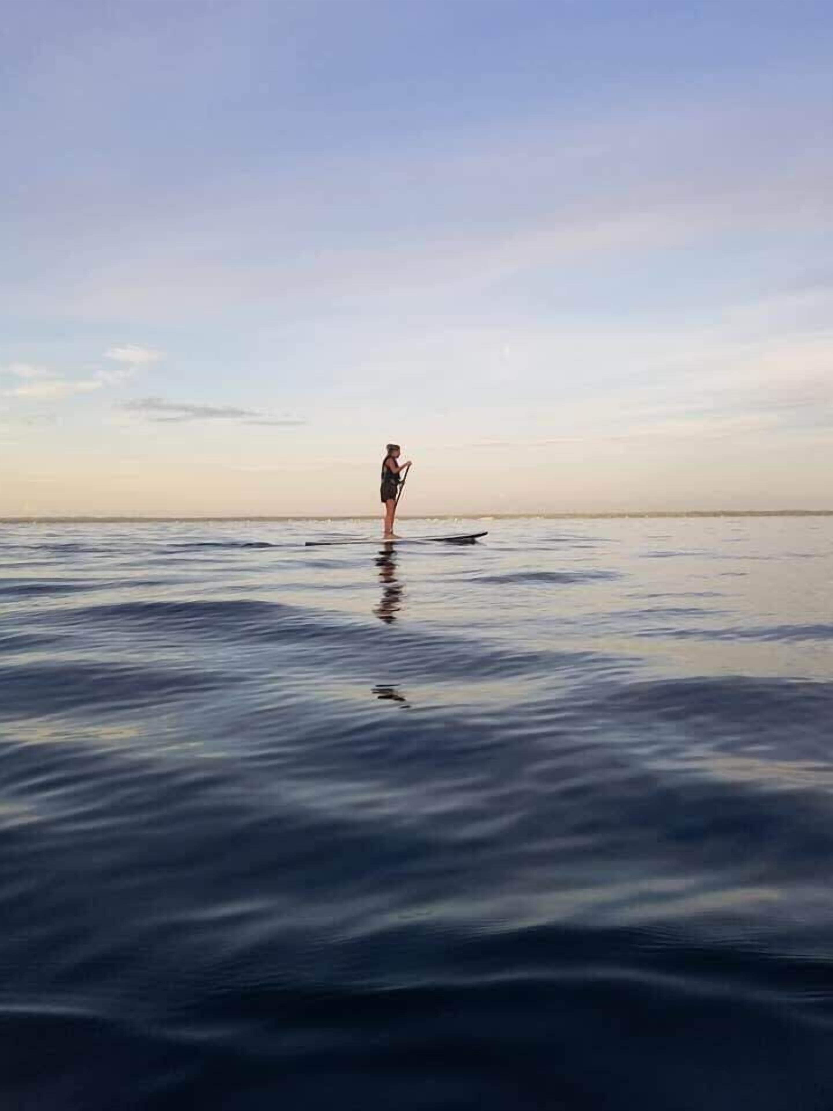 A person standing on a paddleboard in calm water.