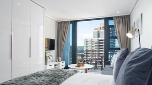 Habitación de hotel moderna con una cama grande, una mesita redonda y un balcón con vistas a la ciudad.