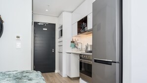Una cocina compacta con armarios blancos, un refrigerador de acero inoxidable y una puerta negra.