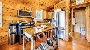 A wooden-paneled kitchen with stainless steel appliances, a wooden table, and hanging pots.