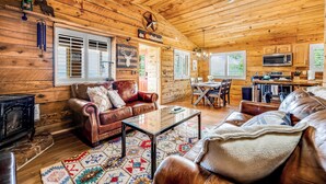 A cozy cabin interior with wooden walls, leather furniture, a fireplace, and a dining area.