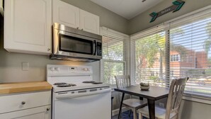 A kitchen with white cabinets, a stainless steel microwave, a white stove, and a dining table with chairs.