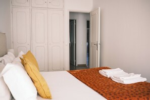 Une chambre d’hôtel avec un lit, un oreiller jaune, une serviette blanche pliée et une armoire.