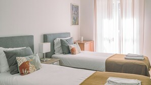 Ein Hotelzimmer mit zwei Einzelbetten, einem Nachttisch mit Lampe, einem kleinen Tisch und einem Fenster mit Vorhängen.