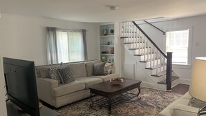 A living room with a sectional sofa, a coffee table, a TV, a staircase, and a bookshelf. - Dock and Boat access Home on the Eastern Shore  Virginia (Belle Haven)