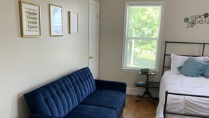Une pièce avec un canapé bleu, un lit avec une literie blanche et une fenêtre donnant sur un paysage verdoyant.