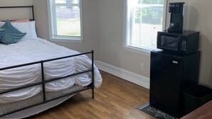 Une chambre avec un lit, un plancher en bois, une fenêtre, un four à micro-ondes et une petite table.