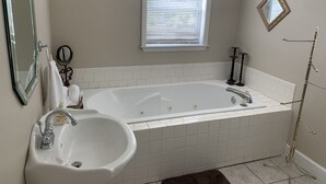 Une salle de bain avec une baignoire blanche, un lavabo, une fenêtre avec des stores et un miroir.