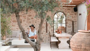 A cozy outdoor seating area with a stone wall, a wooden pergola, and a large planter. - Inotropes Boutique Suites - Adults Only (Archanes-Asterousia)