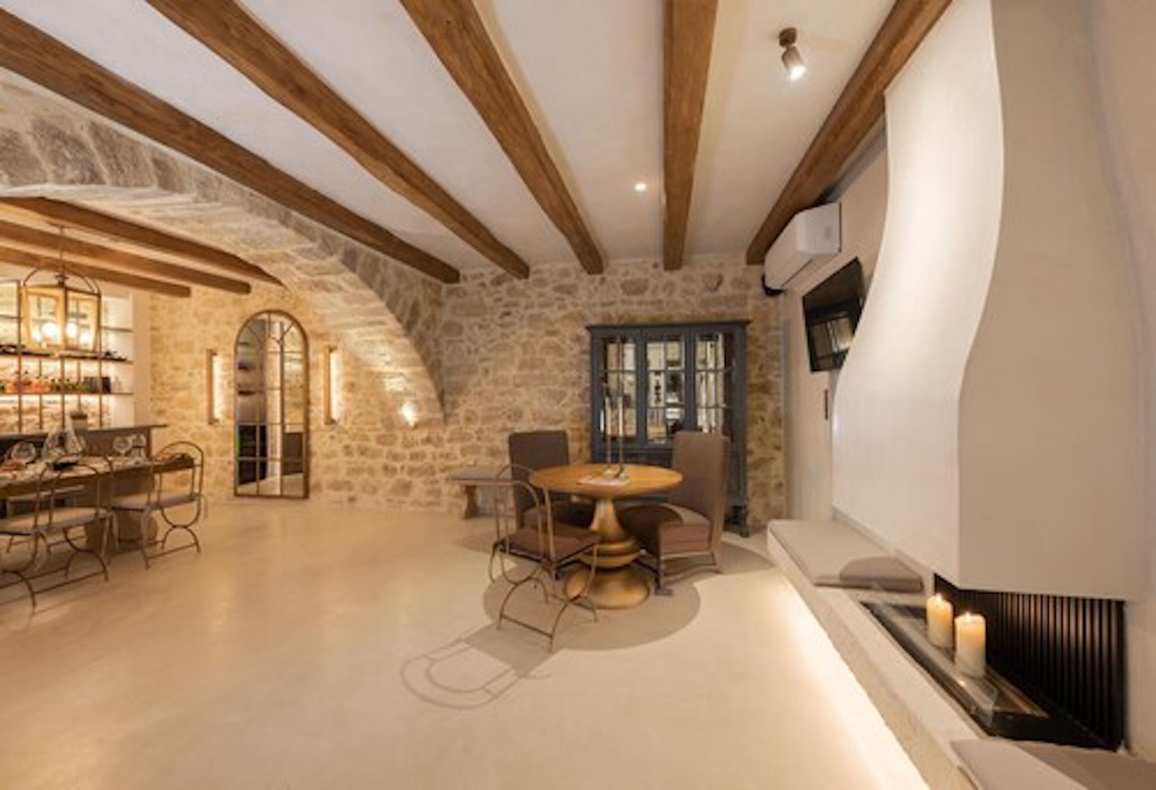 A spacious room with a stone wall, wooden beams, a round table with chairs, and a fireplace.