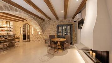 A spacious room with a stone wall, wooden beams, a round table with chairs, and a fireplace.