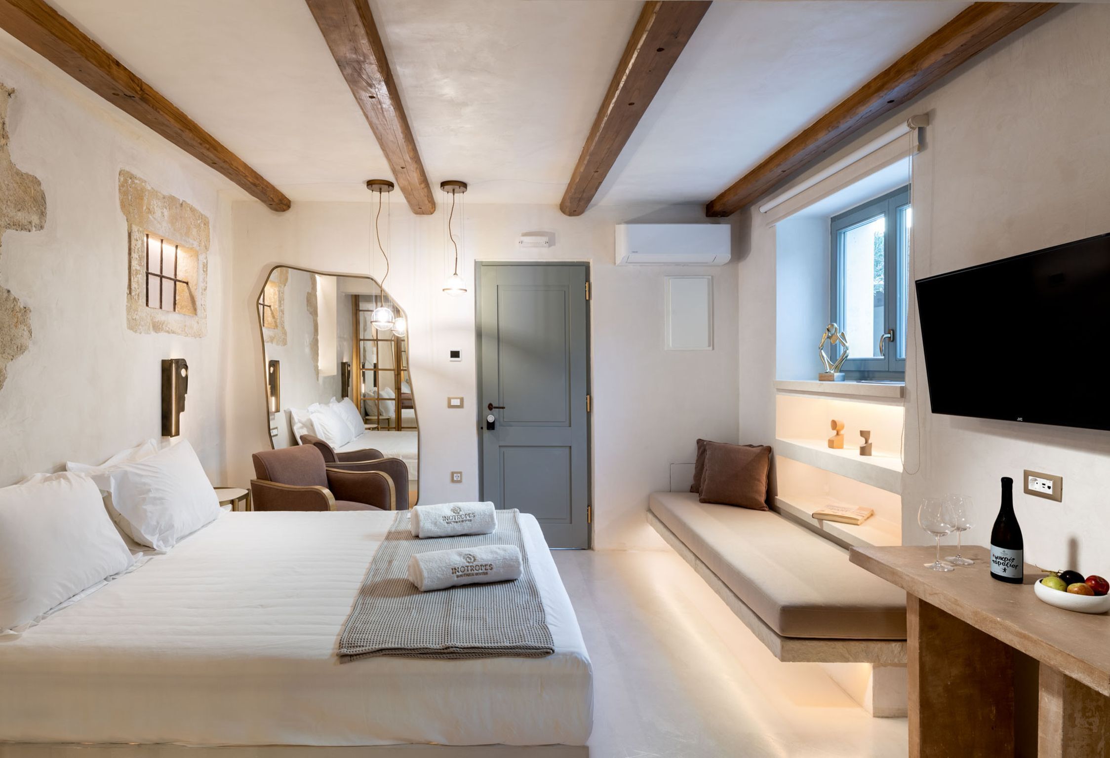 Habitación de hotel con cama, zona de estar, televisor y una pequeña mesa con una botella y vasos.