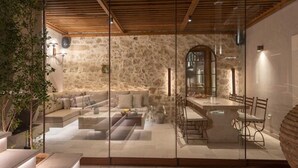 A modern interior with a stone wall, a glass partition, a seating area with cushions, and a dining space with chairs. - Inotropes Boutique Suites - Adults Only (Archanes-Asterousia)