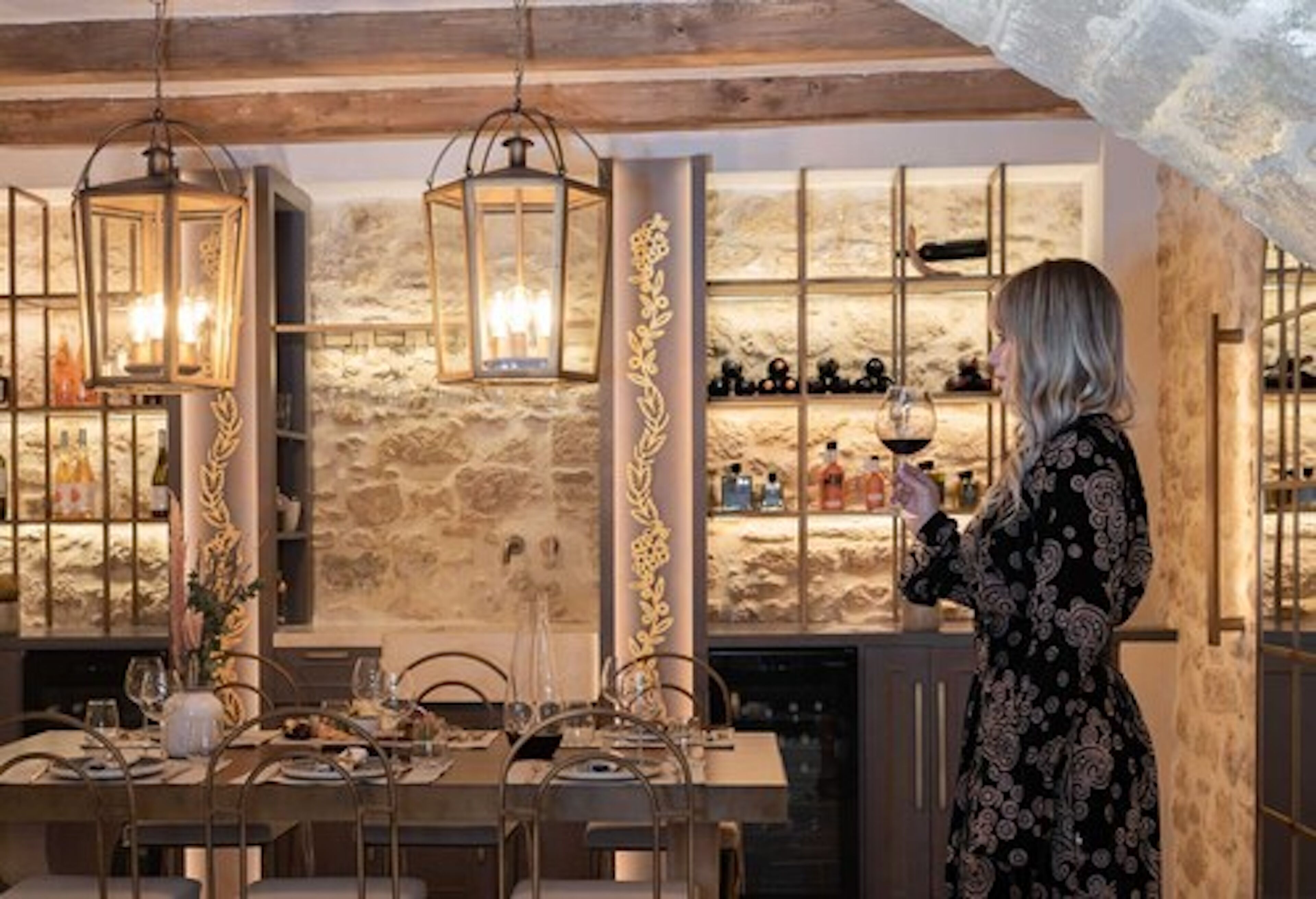A dining area with a stone wall, hanging lanterns, and a wine rack.