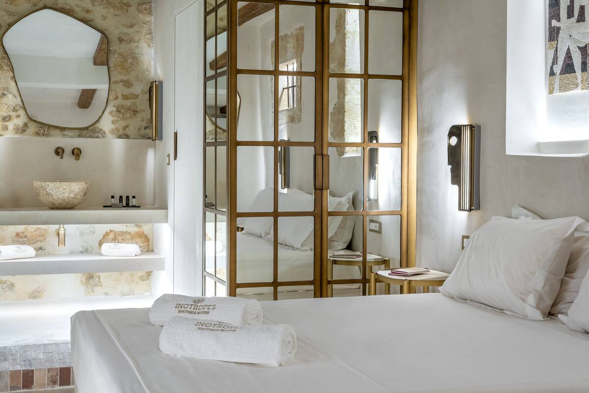 Une chambre d’hôtel avec un grand lit, une salle de bain dotée d’un lavabo en pierre et une vue dégagée grâce à une paroi en verre.
